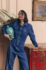 Mono de denim azul con cierre frontal de botones metálicos, cuello camisero, mangas largas y corte de pierna ancha. Incluye bolsillos delanteros y traseros.