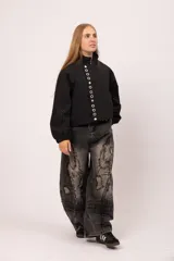 Campera negra de cuello alto con cierre frontal de cremallera y solapa con botones metálicos. Presenta mangas largas con puños elásticos y diseño vanguardista.