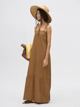 Vestido midi de denim color marrón, con corte holgado, breteles finos con lazos ajustables y detalle de volado en el ruedo.