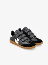 Zapatillas urbanas de cuero blanco con detalles en negro, ajuste con tiras de velcro y suela de goma color caramelo.