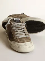Zapatillas deportivas Golden Goose modelo Super-Star, color marrón verdoso desgastado, con estrella lateral negra y detalles en cuero negro en el talón. Presentan un acabado intencionalmente envejecido en la suela y cordones grises. En el lateral se lee el texto 'GGDB/SSTAR'.