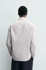 Camisa de corte regular fit confeccionada en tejido de algodón con estampado de cuadros pequeños. Presenta cuello abotonado, manga larga con puños abotonados, bolsillo de plastrón en el pecho y cierre frontal con botones.