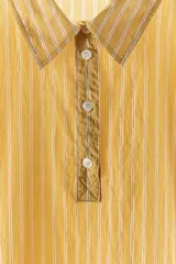 Camisa de corte holgado confeccionada en mezcla de lyocell, con estampado de rayas verticales en tonos amarillos y blancos. Presenta cuello solapa, cierre frontal parcial con botones y mangas anchas por debajo del codo.