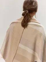 Chal envolvente con diseño de rayas horizontales en tonos beige, tostado y rosado claro, confeccionado en tejido de punto.
