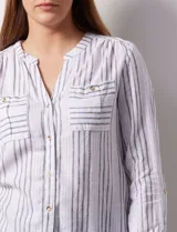 Blusa de lino estampada a rayas verticales en tonos blanco, verde, violeta, amarillo y rosa. Cuello a la base con escote en V y abertura central con botones. Delantera con bolsillos de parche. Mangas largas regulables con presilla y botón.