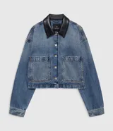 Chaqueta corta de denim azul con cuello camisero de cuero negro y cierre frontal de botones metálicos. Presenta dos bolsillos delanteros con solapa y hombros caídos.