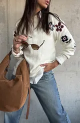 Sweater de punto color natural con cuello redondo y diseño de flores bordadas en las mangas. Presenta puños y ruedo acanalados.
