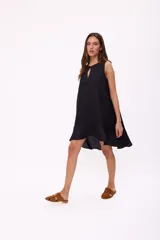 Vestido corto beige de lino, sin mangas, con escote redondo y detalle de abertura en forma de lágrima en el pecho. Presenta diseño holgado y dobladillo asimétrico más largo en la parte trasera con volados.