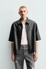 Sobrecamisa de corte relajado confeccionada en tejido efecto piel, con cuello solapa, manga corta y cierre frontal con cremallera. Presenta un bolsillo plastrón en el pecho y bajo con aberturas laterales.