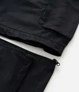 Pantalón cargo de corte mega baggy, color negro, confeccionado en sarga de algodón. Presenta múltiples bolsillos funcionales y un diseño versátil que permite transformar la prenda en bermuda mediante un sistema de ajuste en las piernas.