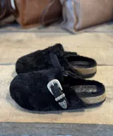 Zuecos negros forrados en corderito sintético, con hebilla metálica decorativa y suela de corcho.