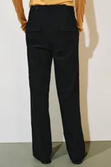 Pantalón de tiro medio color negro con trabillas en la cintura, bolsillos laterales ocultos y pierna recta. Cierre frontal con cremallera, botón y ganchos metálicos.