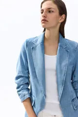 Blazer de denim de algodón celeste, con solapas de muesca, hombreras y mangas tres cuartos fruncidas. Cuenta con bolsillos delanteros con solapa y diseño abierto sin cierre.