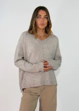 Sweater de punto color gris melange, con escote en V, manga larga y costura central vertical decorativa. Presenta un diseño holgado con terminaciones en tejido acanalado en puños y ruedo.
