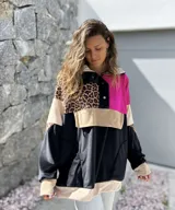 Buzo de estilo canguro con diseño color block que combina paneles en negro, fucsia, beige y un estampado de leopardo. Presenta cuello con cierre de botones a presión y un bolsillo frontal tipo canguro.