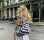 Bolso tote amplio de tela resistente, con diseño de rayas verticales en azul marino y blanco, asas dobles para el hombro y bolsillo frontal.