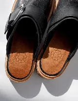 Mules de cuero negro con hebilla plateada y suela color madera.
