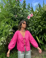 Blusa fucsia de lino con escote en V y mangas largas abullonadas con puños elásticos. Se cierra con lazos en la parte delantera.
