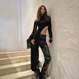 Top negro de manga larga con cuello alto y diseño asimétrico que deja al descubierto un costado del abdomen y cae en un panel largo hasta la rodilla o tobillo.