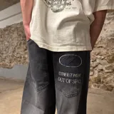 Jean de corte super baggy en color gris oscuro con efecto lavado. Presenta un diseño de pierna ancha y holgada, con bolsillos traseros amplios que incluyen bordados gráficos con texto.