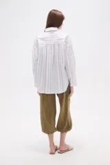 Camisa de algodón con diseño de rayas verticales, corte holgado, cuello camisero, cierre frontal con botones, mangas largas con puños y un bolsillo frontal con rayas horizontales.