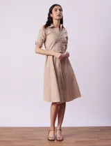 Vestido camisero color beige, marca Sharagano, con cuello con solapa, cierre frontal con botones, mangas 3/4 regulables con presilla y lazo de ajuste en la cintura.