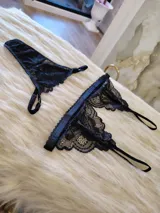 Conjunto de lencería compuesto por un bralette de encaje con breteles regulables y una tanga regulable con corte cola less. Ambas piezas presentan un diseño de encaje floral negro.