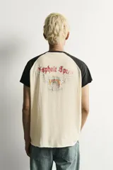Camiseta regular fit de corte clásico con efecto lavado, cuello redondo negro y mangas cortas ranglán negras. El cuerpo es de color blanco con estampa frontal inspirada en automovilismo con el texto "Asphalt Speed".