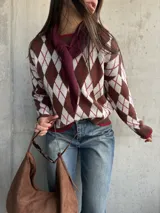 Sweater de tejido de punto con diseño de rombos en tonos chocolate, blanco y detalles en bordó. Presenta cuello redondo, mangas largas y terminaciones acanaladas en puños y ruedo.