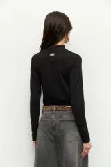 Polera blanca de manga larga con cuello alto y costuras cruzadas a la vista en el frente.