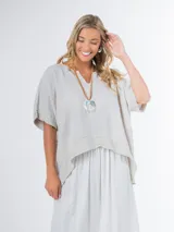 Blusa tipo poncho confeccionada en lino italiano color gris claro, con escote en V y calce amplio.