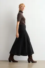 Falda larga de jean color negro, con diseño de paneles verticales y ruedo deshilachado.