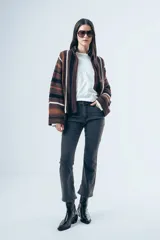 Cardigan de tejido de punto con diseño a rayas horizontales en tonos marrones, negros y blancos. Presenta un corte relajado, cuello alto y mangas largas amplias.