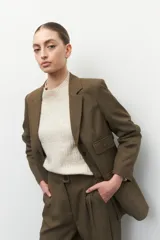 Blazer gris oscuro de corte clásico, con solapas de muesca, cierre con dos botones a tono, bolsillos de solapa decorativos y mangas largas.