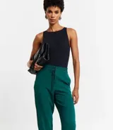 Pantalón de vestir femenino color marrón oscuro, de corte fluido y tiro medio/alto, con cintura elástica ajustable mediante cordón. Presenta bolsillos laterales y cierre frontal.