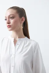 Camisa de color celeste claro con silueta relajada y mangas largas. Presenta un cuello redondo con pequeña abertura frontal y botones, además de un delicado trabajo de tablas en los hombros que aporta textura al diseño.