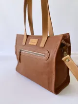 Cartera bandolera de cuero color tostado, con correa larga regulable, bolsillo frontal y forro de tela.