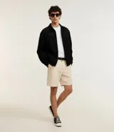 Campera masculina de estilo casual con cuello inglés, cierre frontal por cremallera, bolsillos laterales y ajuste elástico en el bajo. Presenta detalles de recortes en la parte superior delantera.