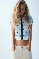 Chaqueta de punto celeste con estampado de estrellas en azul marino, cuello redondo, manga corta y cierre frontal con botones.