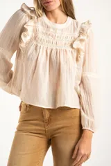 Blusa de color arena con diseño de volados en los hombros, detalle de fruncido en el pecho y mangas largas con puños elásticos.