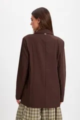 Blazer de corte sastrero en color marrón chocolate, con solapas clásicas, cierre frontal de un botón y bolsillos laterales con solapa.