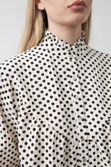 Camisa de viscosa con estampado de lunares, cuello alto con volados y cierre frontal de botones. Presenta un diseño de silueta suelta con frunces que aportan volumen y mangas largas con puños ajustados.