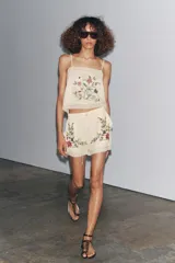 Top color crudo con tirantes finos y escote recto. Presenta bordado floral en el frente y detalle de encaje en el ruedo y escote.