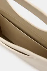 Bolso de mano de piel color rojo, con diseño de cuerpo asimétrico y asa de mano integrada con apertura lateral. Incluye correa bandolera extraíble y bolsillo interior.