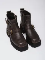 Botas cortas de cuero color marrón, con suela track gruesa y tacón bajo. Presentan correas decorativas con hebillas metálicas doradas en el tobillo y cierre lateral para mayor comodidad.