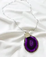 Collar con cadena de eslabones plateada y dije de piedra ágata color púrpura con engarce plateado.