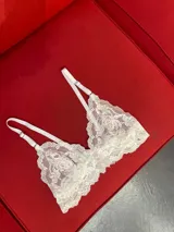 Bralette de encaje blanco con diseño floral, tirantes regulables y terminaciones festoneadas.