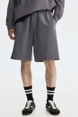 Short de felpa interlock color gris oscuro, con cintura elástica fruncida y cordón ajustable. Presenta un diseño de corte relajado a la rodilla, bolsillos laterales y bolsillos traseros.
