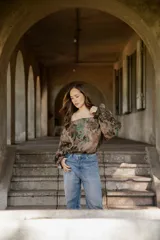 Blusa de lino con diseño off-shoulder, mangas largas amplias y estampado floral en tonos tierra y verdes.