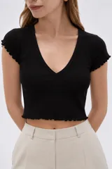 Remera de manga corta color negro, confeccionada en algodón con elastano, de tejido acanalado, corte al cuerpo y escote en V con detalles de volados en las terminaciones de mangas y ruedo.